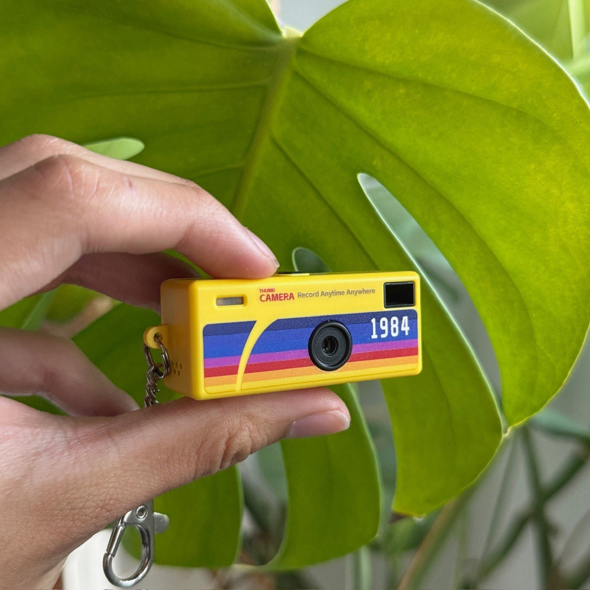 Keychain Digicam held between two fingers to show its thumb-sized scale